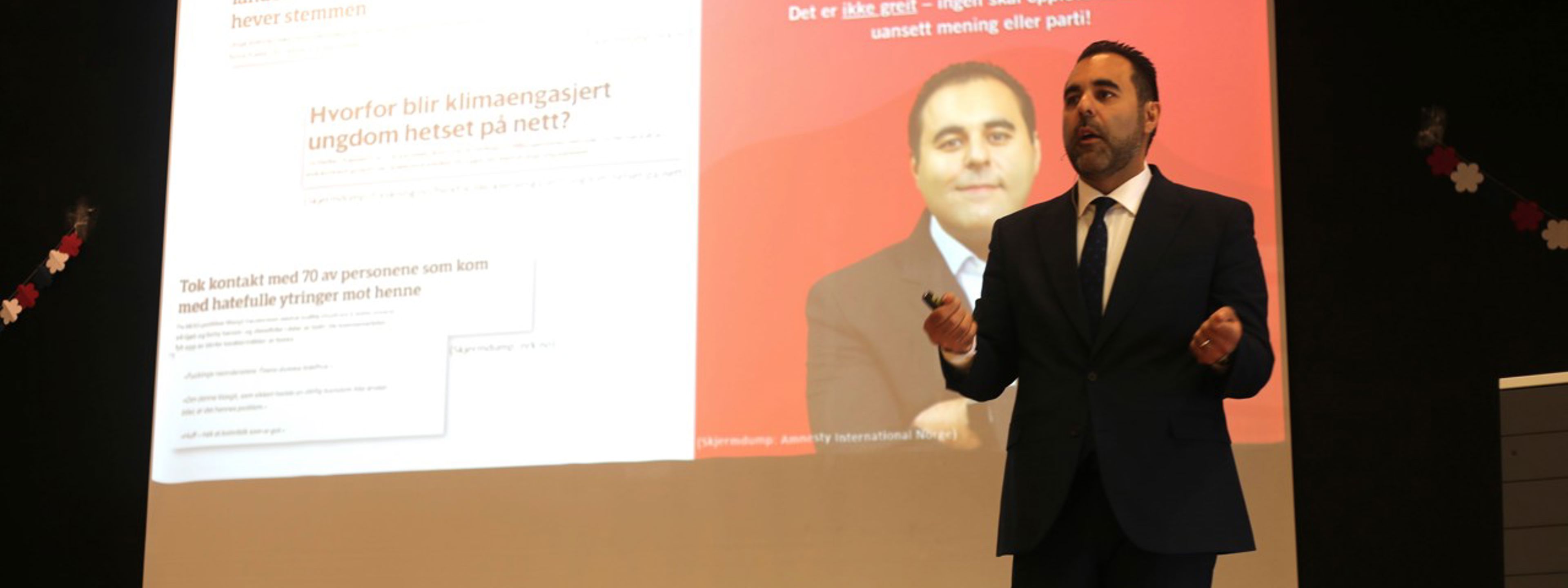 Stortingspresident Masud Gharahkhani står på scena framfor eit bilete av seg sjølv og kva han er oppteken av.