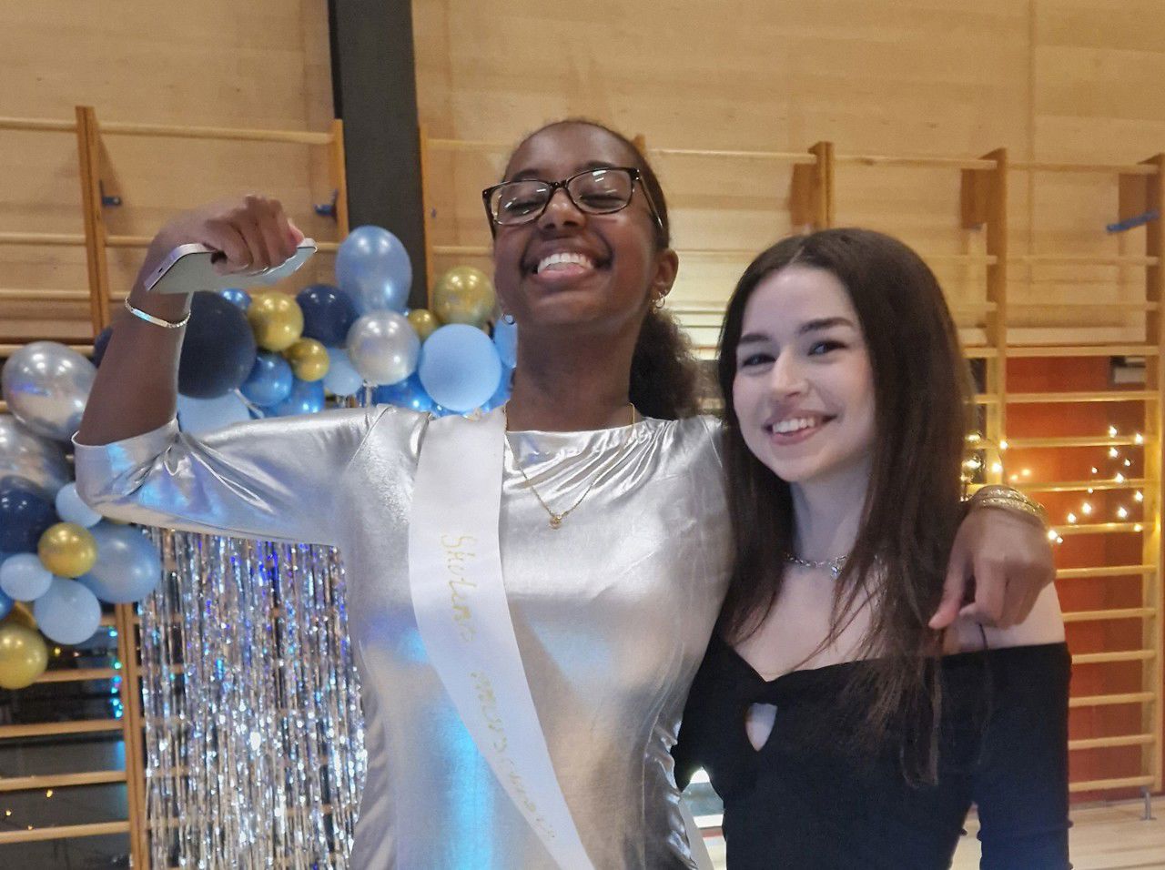 Ei jente i sølvfaga kjole og ei jente i svart kjole som held rundt kvarandre