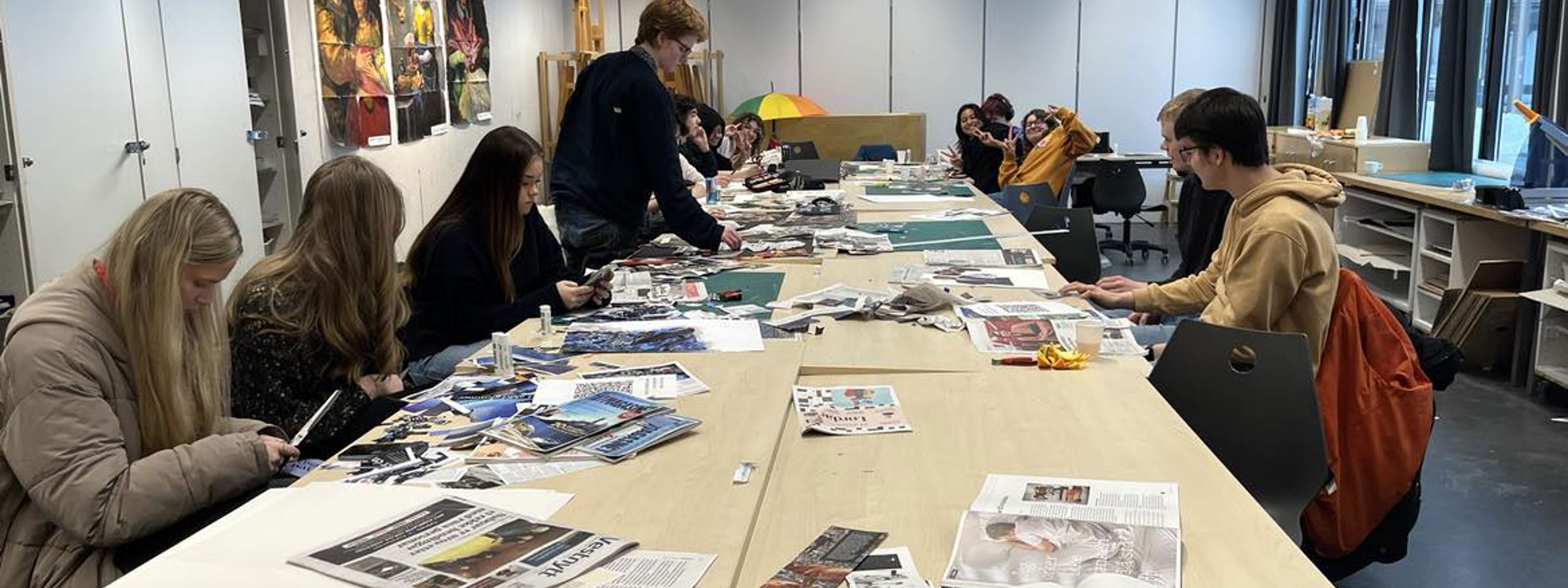 11 elevar sit ved eit langbord og klippar i aviser og vekeblad