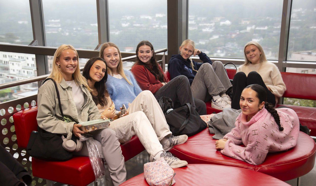 7 elevar sit i ein raud sofa og ser mot fotografen