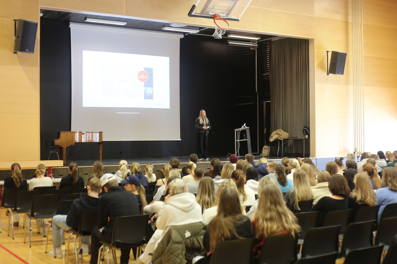 Emma Ingebrigtsen står på scena i gymsalen og snakkar til alle elevane