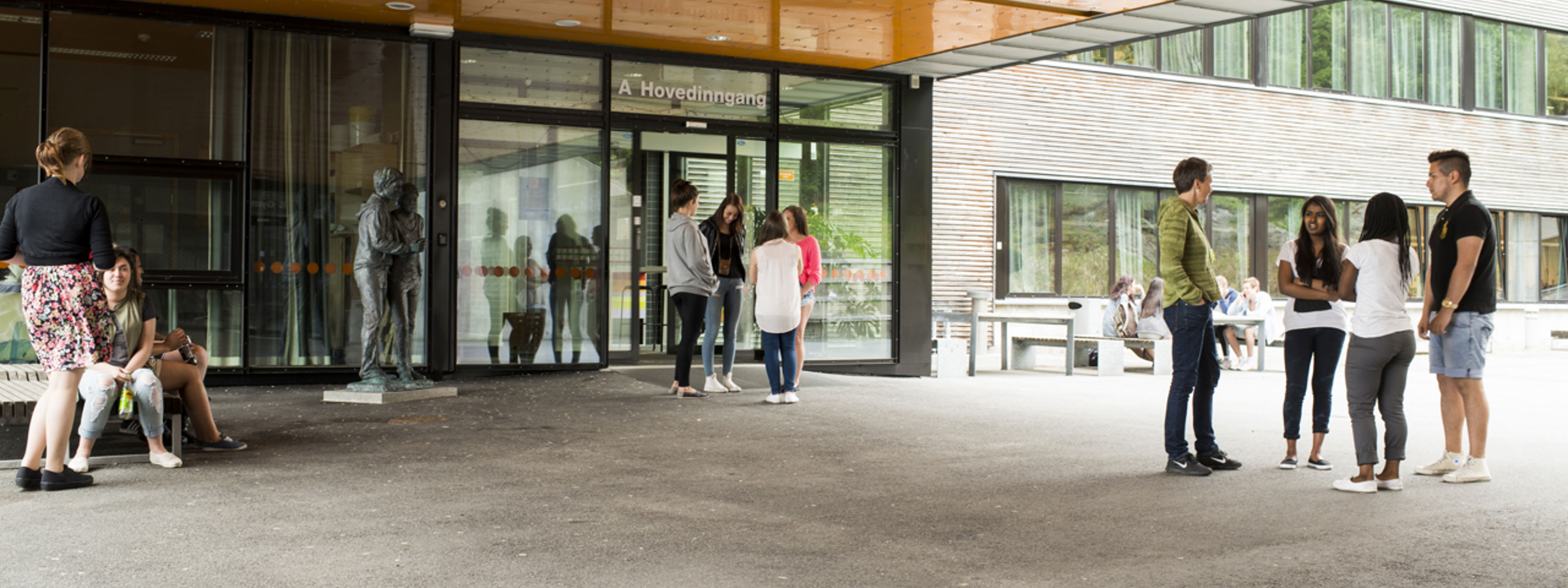 Ungdomar står i grupper ved inngangspartiet ved Olsvikåsen vgs