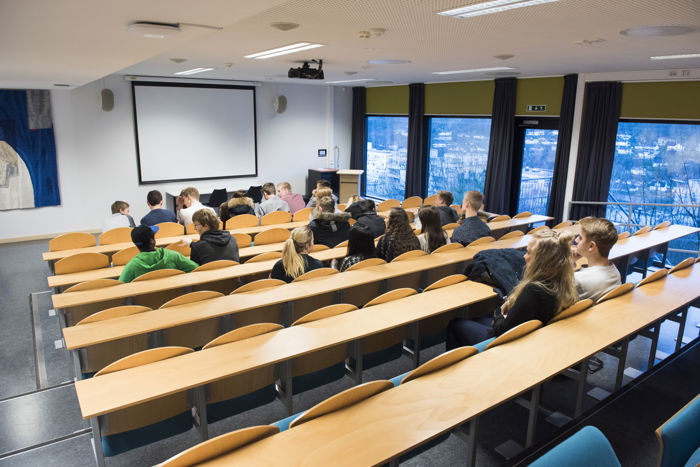 Elever som sit og ser fram på ei tavle i eit auditorium
