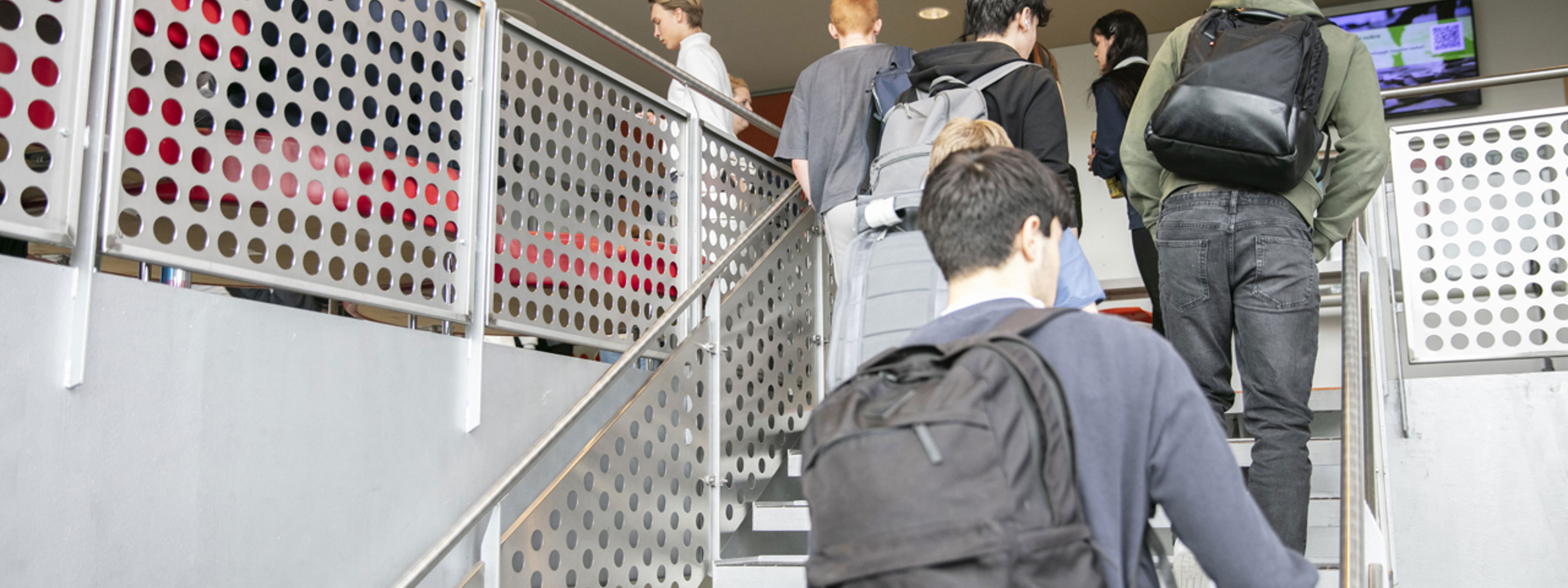 Elevar med skulesekk på ryggen som går opp trappa inni skulen