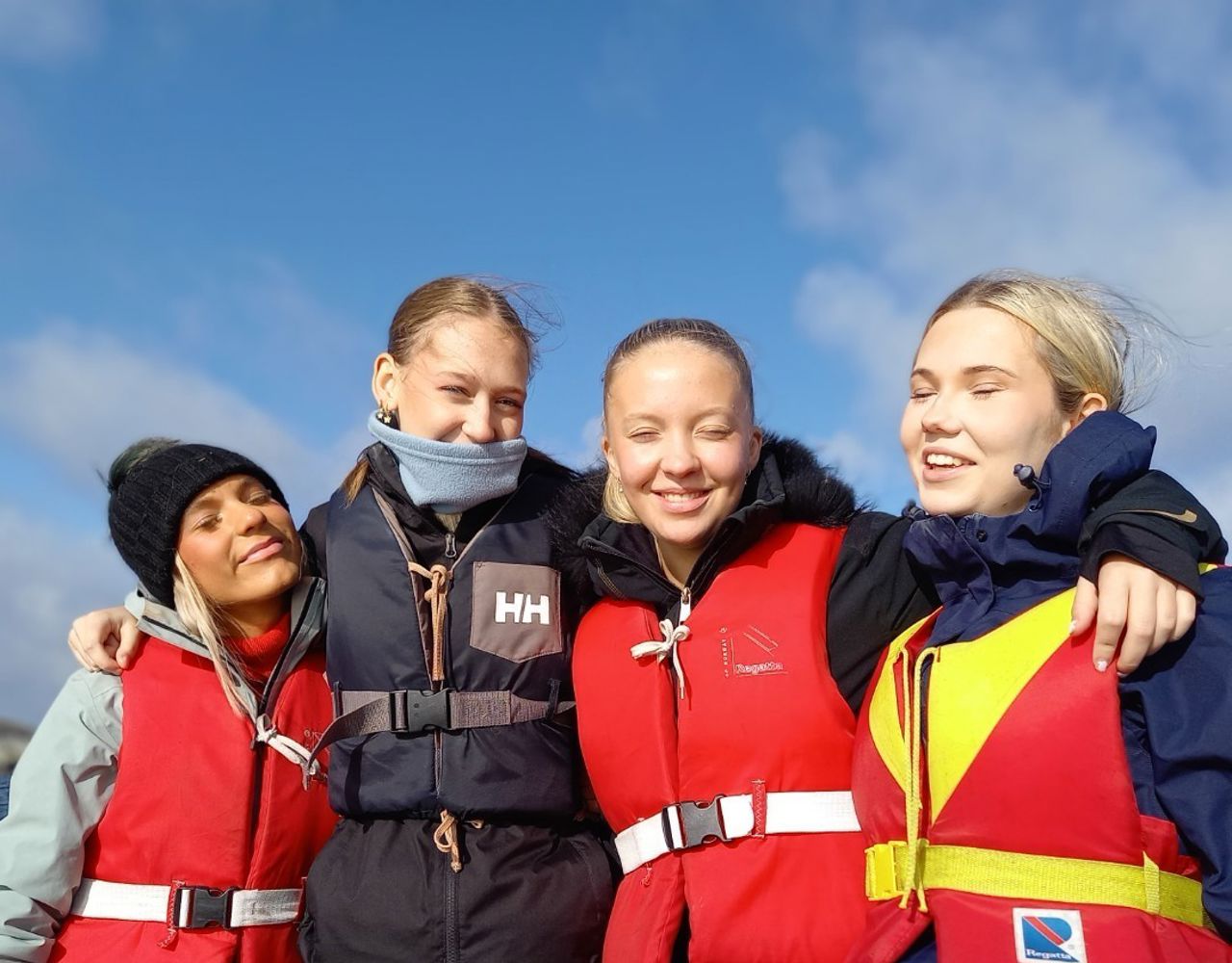 4 jenter som står tett saman med redningsvestar på