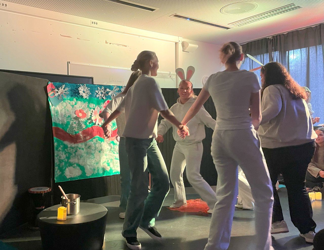 Elevar som dansar i ring  framfor eit stort malt elevarbeid utklipp i papir av samiske flagg og blomster