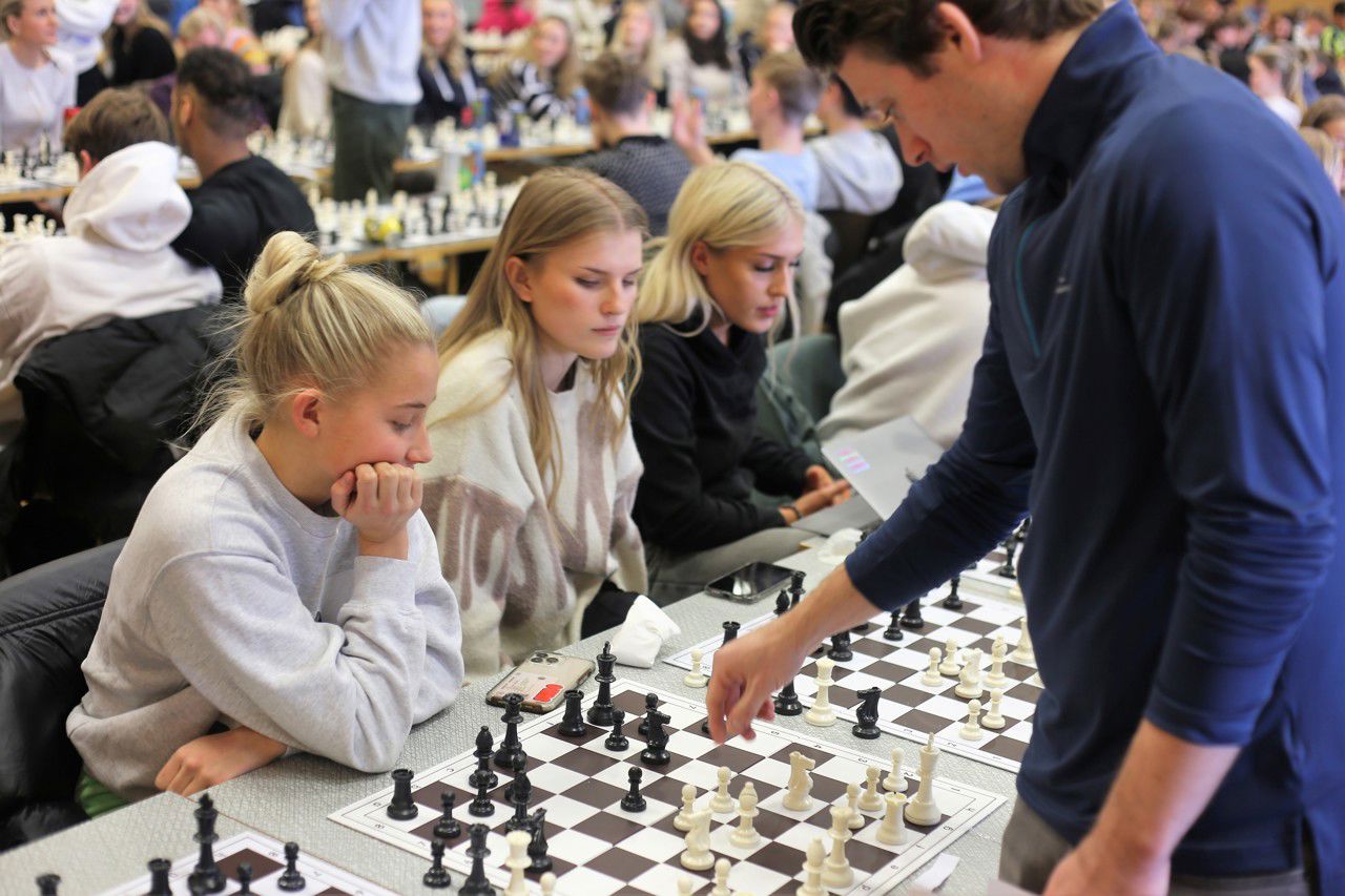Joachim B. Nilsen som flyttar sin sjakkbrikke framfor brettene til tre jenter
