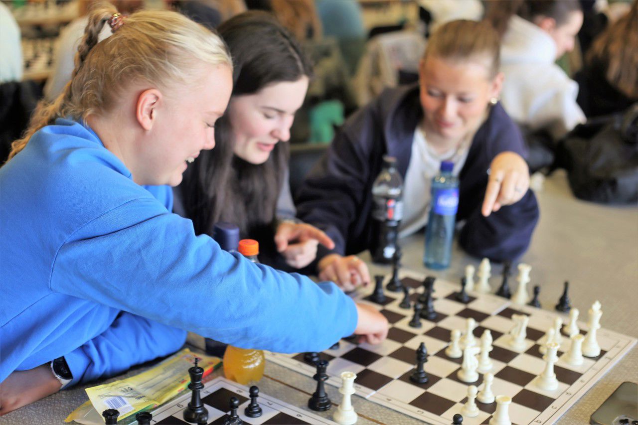 Tre jenter diskuterer sjakk spelet over sjakkbrettet