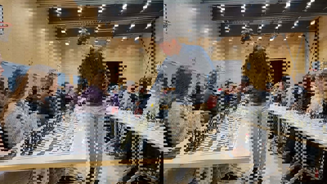 En sjakk spelar går langs eit lanbord med mange sjakk brett på og spelar med elevane