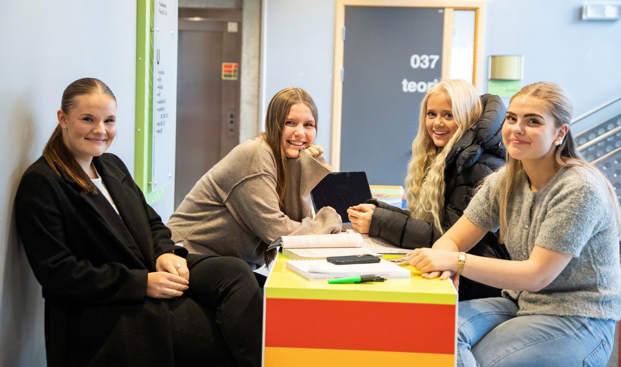 Fire smilande jenter sit rundt eit bord og jobbar med skulearbeid