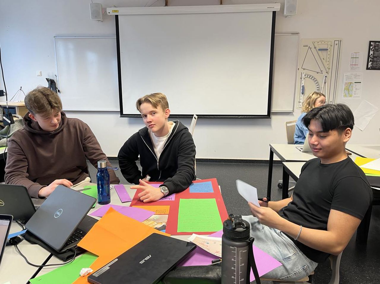Tre gutar sit i klasserommet og lagar fargerikt plakatar til Demokratidagen