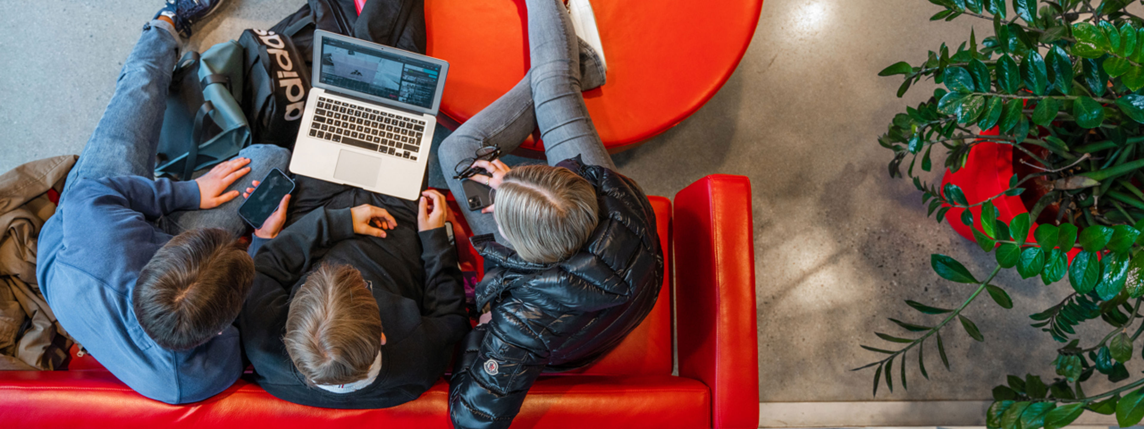 Tre elevar sit i ein raud sofa og ser på en pc.