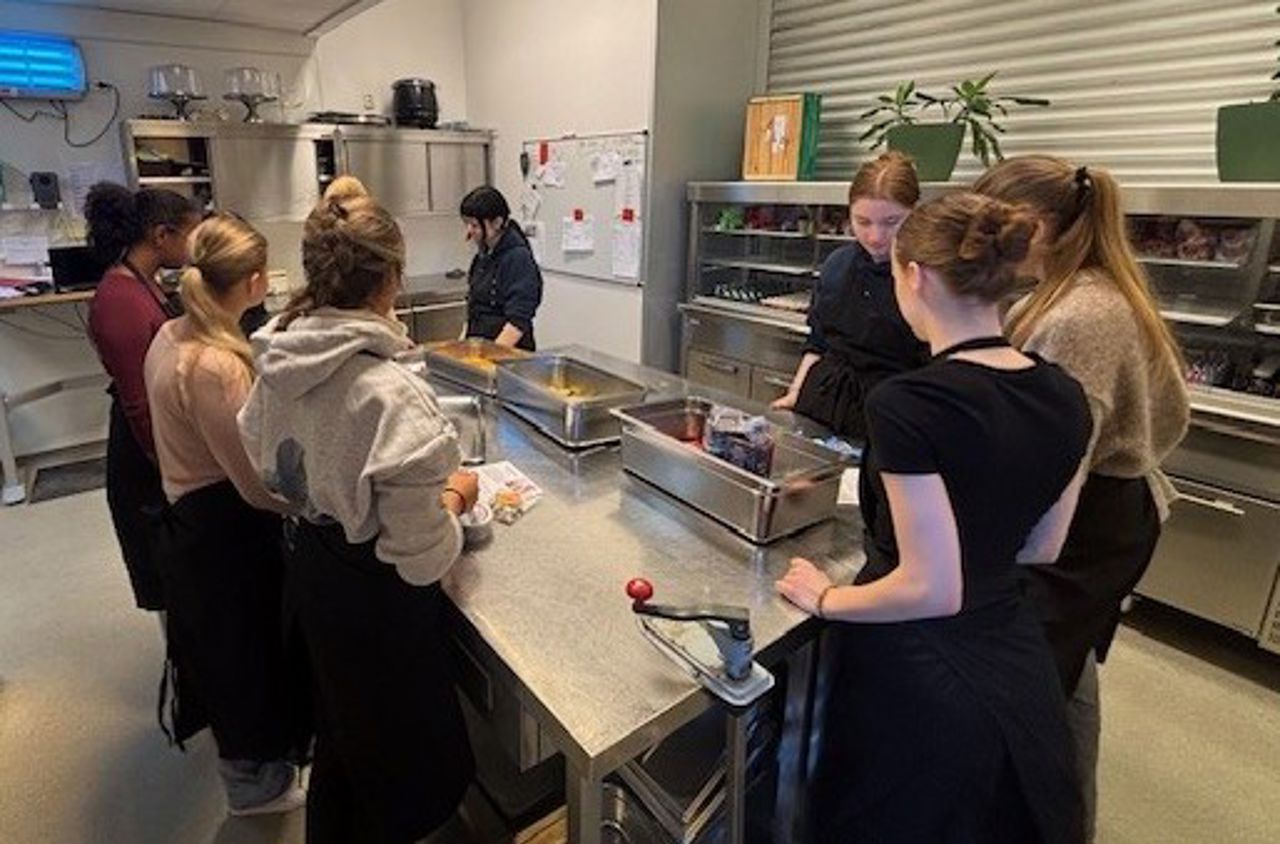 Sju elevar står og lagar mat ved ei kjøkkenøy