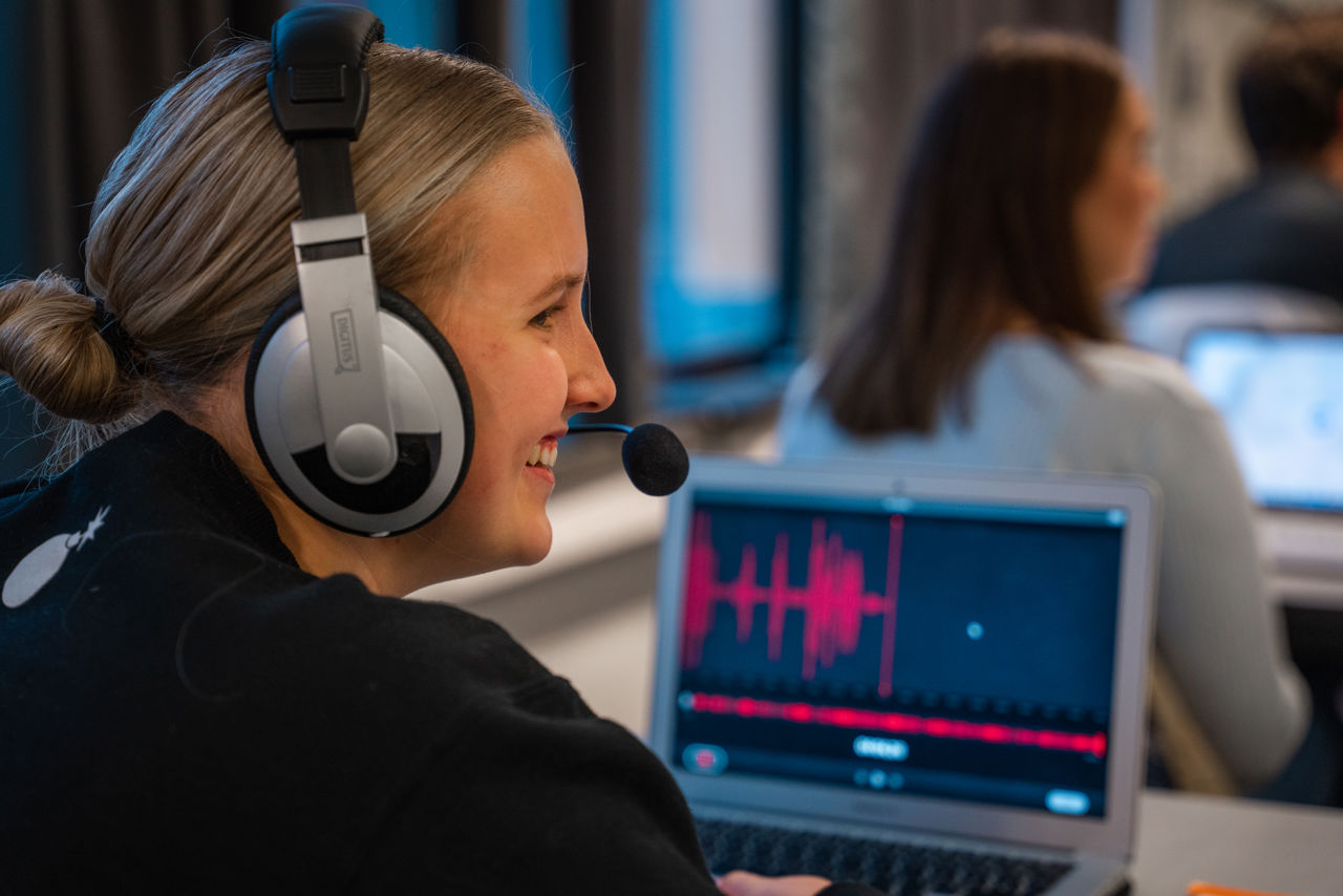 Elev med hodetelefonar sit framfor ein PC