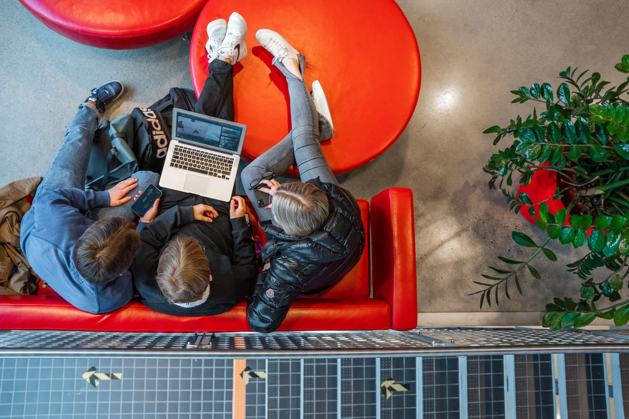 3 elevar som sit i ein raud sofa og ser på ein pc