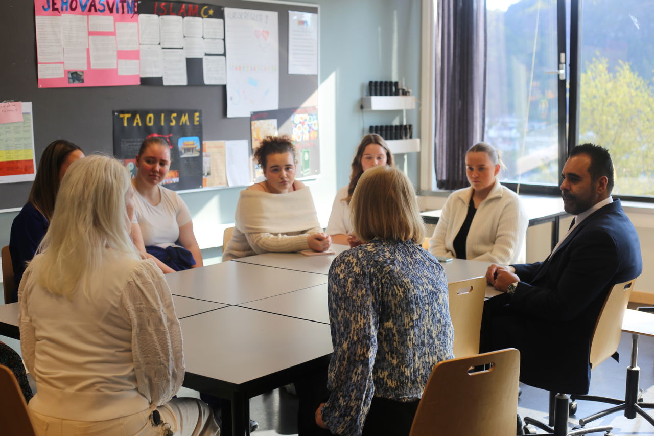 Stortingspresidenten sit rundt eit bord saman med skulens Helse og oppvekst elevar og snakkar