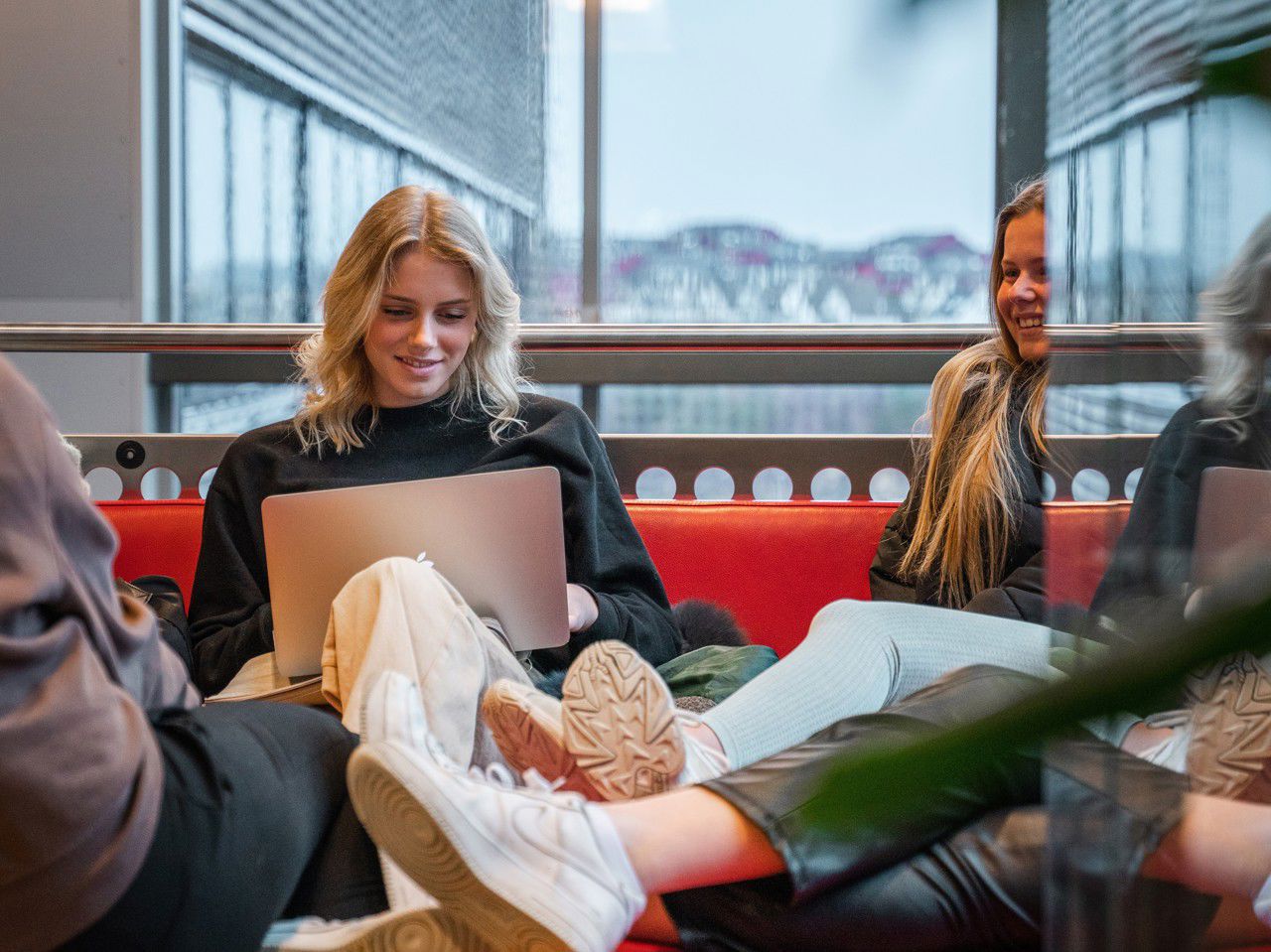 Ein elev sit i ein raud sofa med pc på fanget
