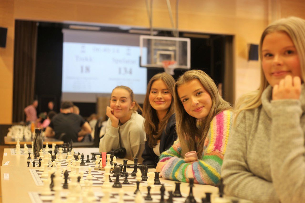 Fire jenter sit ved sjakkbordet og smilar