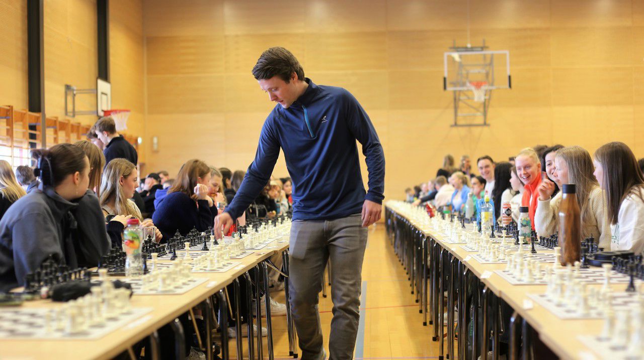 Joachim B. Nilsen går langs rekken med sjakkbrett og spelar mot elevar