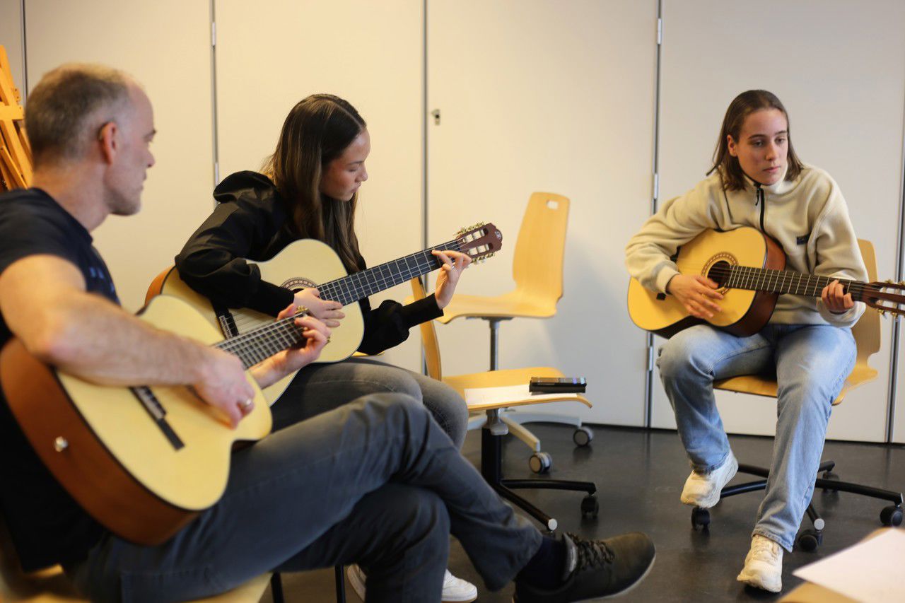 To elevar og ein lærar sit å spelar gitar